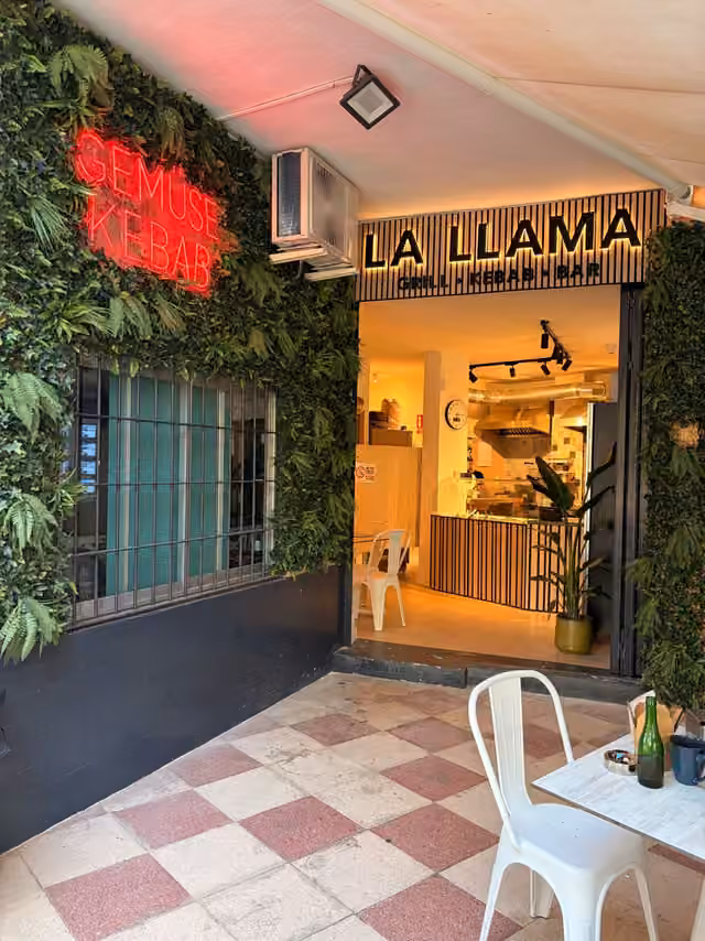 Entrada de La Llama con terraza, pared verde y letrero iluminado